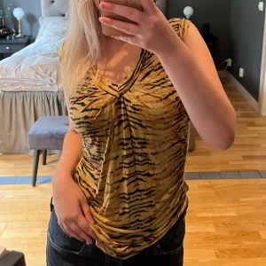 Tigermönstrad topp från Zara - Säljer en snygg tigermönstrad topp från Zara i storlek M. Den är ärmlös och har en v-ringad design som ger en cool look. Toppen är i ett mjukt och bekvämt material. Väldigt stretchig.
