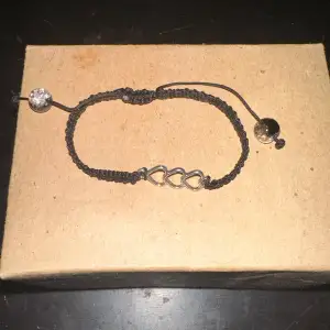 Säljer ett snyggt svart armband med flätad design och tre silverfärgade hjärtan i mitten. Armbandet har justerbar knytning med en glittrig pärla i änden. Perfekt för att ge en stilren touch till din outfit!