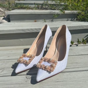 Vita pumps med spetsig tå och strass/pärldetalj - Säljer ett par eleganta vita pumps i ett lite skimmrigt tyg, med spetsig tå och smal klack. Skorna har en vacker dekoration framtill med pärlor och glittrande stenar, liknar manolo blahnik. Perfekta för fest, i storlek 40 men närmare storlek 39. 