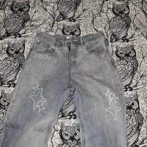 Gråa jeans från Broken Planet Market - Snygga grå jeans med unika vita stjärnmönster och texten 'BROKEN' broderad på framsidan. Jeansen är knappt använda, dem är som nya. Perfekta för en cool och avslappnad stil. Storleken är W28 - L30, passar mig som är 178cm och 70kg. 