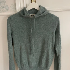 Grå hoodie från Soft Goat - Mysig grå hoodie från Soft Goat i kashmir. Tröjan har en klassisk design med huva och dragsko, samt ribbade muddar vid ärmslut och nederkant. Perfekt för kyliga dagar.