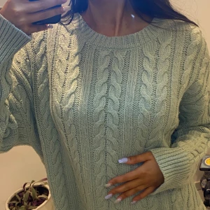 Grön stickad tröja - Mysig grön stickad tröja med kabelstickat mönster. Perfekt för kyliga dagar med sin avslappnade passform och långa ärmar. En klassisk och stilren design som passar till många tillfällen.