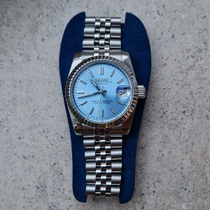 Seiko Mod Oyster Perpetual Datejust Sky Blue - Seiko-mod inspirerad av den ikoniska Oyster Perpetual Datejust, med en fantastisk himmelsblå urtavla. Klockan är helt oanvänd och i perfekt skick. Med sitt 36 mm stora boett är den den perfekta storleken för alla handleder. Som den enda mod-tillverkaren som använder Seiko-crowns i mina byggen har denna klocka en unik detalj som skiljer den från andra. Skickas från Sverige 🇸🇪