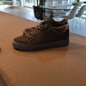 Gråa sneakers från The Garment Project - Snygga gråa sneakers i mocka från The Garment Project. Skorna har en klassisk design med snörning och en robust sula. Perfekta för en stilren vardagslook. Super fint skick!   Tveka inte på att skriva om du har funderingar!