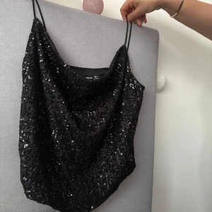 Svart paljettlinne  - Snyggt svart linne täckt med glittrande paljetter. Linnet har tunna axelband och en lös passform, perfekt för festliga tillfällen. Ett måste för garderoben om du vill sticka ut!