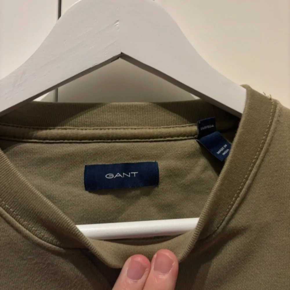 Säljer en stilren olivgrön sweatshirt från GANT. Tröjan har en klassisk rund halsringning och långa ärmar. Perfekt för en avslappnad look. Passar bra till både jeans och chinos.. Neuletakit & Villapaidat.