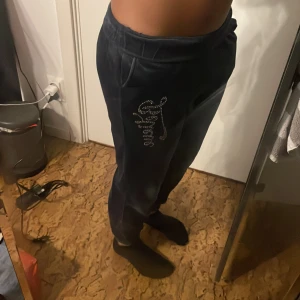Mörkblå mjukisbyxor med bling från Lindex - Säljer ett par mörkblå mjukisbyxor i sammet från Lindex med texten 'Believe' i glittriga stenar på sidan. Byxorna har resår i midjan och vid bensluten för extra komfort. Perfekta för en avslappnad men samtidigt festlig stil