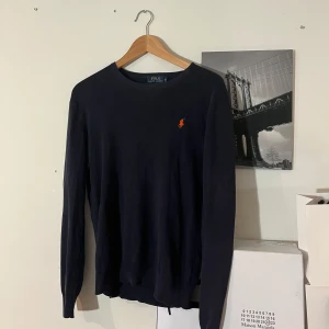 Mörkblå tröja från Polo Ralph Lauren - Snygg mörkblå tröja från Polo Ralph Lauren med den ikoniska loggan i orange på bröstet. Tröjan har en slim fit passform och är perfekt för en stilren look. Den är långärmad och tillverkad i ett mjukt material.passar perfekt att ha till skolan✅😁