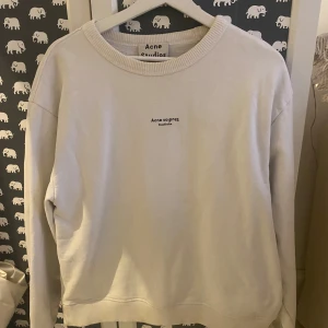 Vit sweatshirt från Acne Studios - Säljer en stilren vit sweatshirt från Acne Studios. Tröjan har en rund halsringning och Acne Studios-loggan tryckt på bröstet. 
