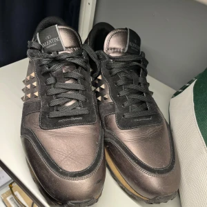 Valentino Garavani sneakers  - Snygga Valentino Garavani sneakers i en cool metallicfärg med svarta detaljer. Skorna har den ikoniska rockstud-designen på sidorna och svarta snören. Köpta av ett företag kvitto finns 