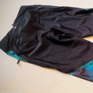 Svarta och turkosa leggings med galaxmönster - Unika coola trekvarts leggings i svart och turkos med ett coolt galaxmönster. De har en praktisk dragkedja baktill för förvaring till när du är ute på din löprunda eller bara chillar hemma eller någon helt annanstans. Super sköna stretchiga airflow thigts som passar både till träning eller en vanlig dag på stan. Perfekta för att ge din outfit en unik och färgglad touch. Dem är helt nya och aldrig använda. 