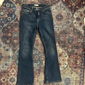 Blå bootcut jeans - Ett par mörkblå bootcut jeans med medel hög midja. De är från ginatricot, endast använt ett fåtal gånger därav de slitna änderna, men det syns ej när man bär de. De är väldigt stretchiga och väldigt sköna, i storlek 40.