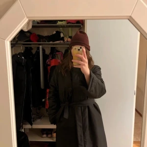 Svart parkajacka från Filippa K - Säljer en stilren svart parkajacka från Filippa K. Jackan har en praktisk huva och knytskärp i midjan för en justerbar passform. Perfekt för kyliga dagar med sin långa design och bekväma passform.