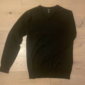 Svart tröja från Callaway - Säljer en stilren svart tröja från Callaway. Tröjan har en v-ringad hals och långa ärmar, perfekt för en klassisk look. Den är tillverkad i ett mjukt material som ger en bekväm passform.