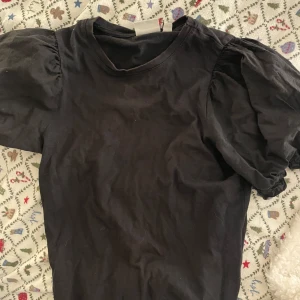 Svart topp med puffärmar från Vila - Snygg svart topp från Vila med puffiga kortärmar. Perfekt för en stilren look. Tillverkad i mjukt material för extra komfort.