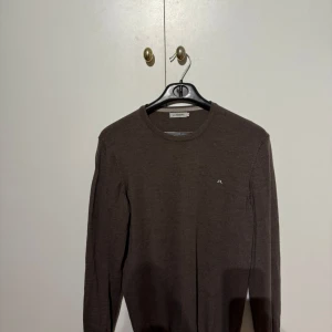 Brun Merinotröja från J.Lindeberg - Säljer en stilren brun tröja från J.Lindeberg i 100% merinoull. Tröjan har en diskret logga på bröstet och rund halsringning. Perfekt för kyligare dagar. Storlek M