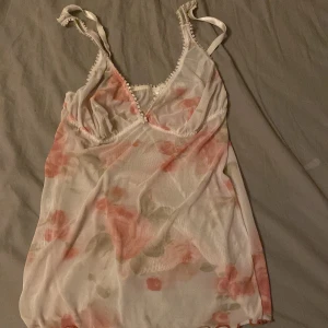 Blommig linne i mesh - Säljer ett romantiskt linne i mesh från Victoria's Secret. Det har ett blommigt mönster i rosa och beige toner med spetsdetaljer och justerbara axelband. Perfekt för en somrig look!
