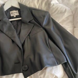 Svart skinnjacka från NA-KD - Snygg svart skinnjacka från NA-KD med en croppad design och knappar framtill. Perfekt för en trendig look.