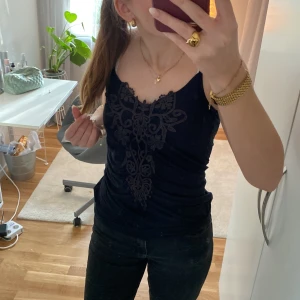 Svart linne från Zoul - Snyggt svart linne från Zoul med tunna axelband och vacker spetsdetalj framtill. Perfekt för en stilren look.