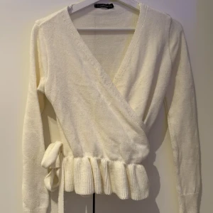 Vit omlottkofta från Boohoo - Säljer en stilren vit/offwhite omlottkofta från Boohoo. Koftan har långa ärmar och ett knytband i midjan för en justerbar passform. Den är ribbad vid nederkanten vilket ger en fin detalj. Perfekt för lager-på-lager under kyligare dagar.