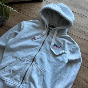Superdry zip hoodie - Säljer en grå hoodie från Superdry med dragkedja och huva. Den är oerhört skön och sitter asbra. Dock använd max 5 gånger då den är för liten för mig. Det är tjockt material så den är perfekt nu till vintern
