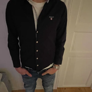 Svart GANT Skjorta - Säljer en Svart GANT Skjorta. Storleken är 152-158 men han på bilden är ca 168 cm lång och passar honom perfekt! Kontakta och skriv gärna vid frågor eller intressen!