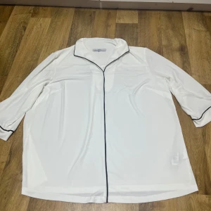 Vit blus med svarta detaljer - Elegant vit blus med svarta kantdetaljer. Blusen har trekvartsärmar och en klassisk krage. Perfekt för en stilren look. Priset går att diskuteras