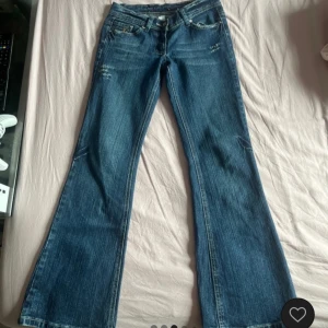 Blå bootcut jeans med detaljer - Snygga mörkblå bootcut jeans med slitningar och dekorativa detaljer på bakfickorna.             Bilderna är ifrån säljaren jag köpte dem av på vinted så det är ej jag på bilden ✨Säljer då de är för små för mig. Mått - midja: 32cm innebenslängd: 66cm