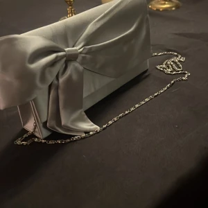 Elegant silverfärgad väska med rosett - Snygg och stilren kuvertväska i silver med en elegant rosett på framsidan. Väskan har en kedja för axelrem och en praktisk dragkedja inuti. Perfekt för festliga tillfällen eller en utekväll. Väskan är i mycket bra skick och redo att användas! Pris kan diskuteras🎀🩷