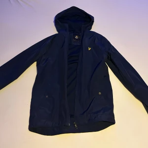 Mörkblå vindjacka med huva - Säljer denna mörkblå vindjacka från Lyle & Scott. Bra skick inga skador eller slitningar. Nypris 1099kr.  Hör gärna av dig med frågor eller andra funderingar. 