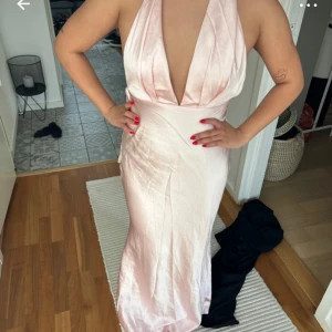 Ljusrosa sidenklänning - Säljer en elegant ljusrosa långklänning i siden med djup v-ringning och öppen rygg. Perfekt för festliga tillfällen! Klänningen har en vacker drapering och knytning i nacken. Den är i nytt skick och ger en lyxig känsla. Helt ny med prilapp, nypris 1000kr