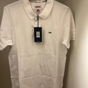 Vit pikétröja från Tommy Jeans - Säljer en klassisk vit pikétröja från Tommy Jeans i storlek M. Tröjan är i helt nytt skick.                           Nypris 750kr! 