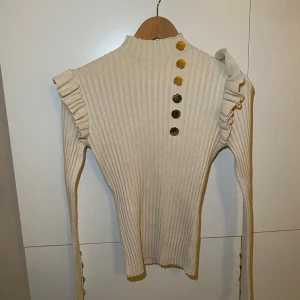 STICKAD LÅNGÄRMAD TRÖJA  - En jätte fin/söt krämvit långärmad som är stickad. Den har  fina guld detaljer & volanger längst uppe vid ärmen. Fint skick. 