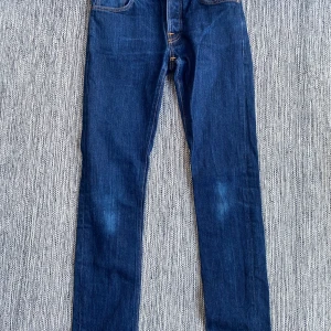 Mörkblåa jeans W30/L34 från Nudie Jeans modell Grim Trim - Mörkblåa jeans W30/L34 från Nudie Jeans modell Grim Trim.  Sparsamt använd och i fint begagnat skick.  Mått Midjan: ca 39 cm Längd från grenen och ner: ca 82 cm  98% bomull och 2% elastan  Kommer från ett djur och rökfritt hem.