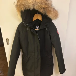 Svart parkajacka från Canada Goose - Säljer min fina canada goose jacka i modellen viktoria parka pga den inte längre passar min stil eller storlek. STORLEK M.