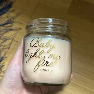 Doftljus i ljuvlig vanlijdoft - Säljer ett doftljus i en söt glasburk med texten 'Baby light my fire' i guld. Doften är 'Candy Floss' och ljuset har en ljusrosa färg. Perfekt för att skapa en mysig stämning hemma! 🕯️