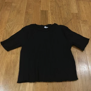 Svart ribbad topp från Stories - Säljer en svart ribbad topp från Stories i storlek M (40-42). Toppen har trekvartsärmar och en enkel design som passar perfekt till både vardag och fest. Den är i bra skick och superbekväm att ha på sig. Perfekt för höst och vår!