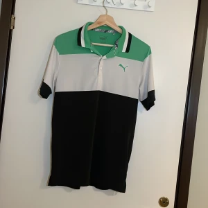 Grön och svart pikétröja från Puma - Säljer en snygg pikétröja från Puma i grönt, svart och vitt. Perfekt för både vardag och träning. Tröjan har en klassisk krage med knappar och korta ärmar. Den är i mycket bra skick och redo för nya äventyr! Pris går alltid att förhandlas!