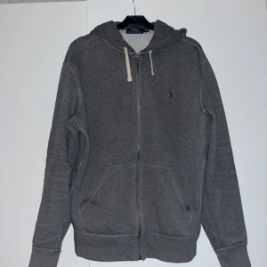 Grå hoodie från Polo Ralph Lauren - Säljer en snygg grå hoodie från Polo Ralph Lauren i mycket bra skick. Den har en dragkedja framtill och praktiska fickor. Perfekt för höst och vinter, och den är supermjuk och bekväm. Passar både till vardags och chillkvällar. 