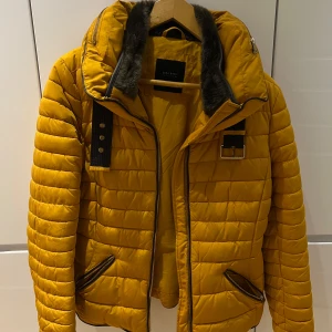Vinterjacka från Zara - Säljer en snygg gul jacka från Zara. Den har en mysig fuskpäls vid kragen och coola dragkedjor. Jackan har en normal passform och är i mycket bra skick!!!! 