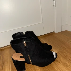 Svarta mocka boots med klack - Snygga svarta boots i mocka med öppen tå och dragkedja på sidan. De har en stabil klack som ger lite extra höjd utan att kompromissa med komforten. Perfekta för både vardag och fest! HELT OANVÄNDA