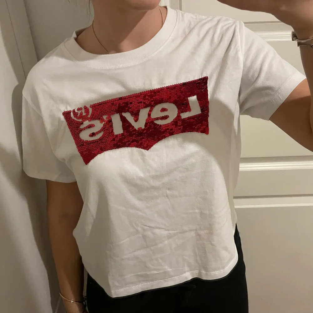 Säljer en snygg vit t-shirt från Levi's med ett coolt rött paljettmönster på bröstet. Perfekt för att ge din outfit lite extra bling! T-shirten är kortärmad och i bomull, vilket gör den superbekväm att ha på sig. Passar perfekt till både vardag och fest. 🕺✨ skriv vid frågor och priset kan diskuteras💓. T-paidat.