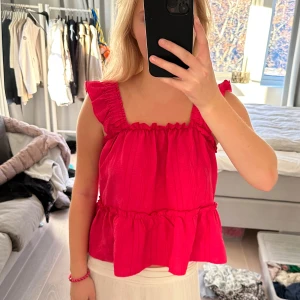 Rosa volangtopp - Säljer en superfin rosa topp med volanger. Den är ärmlös och har en luftig passform, perfekt för sommardagar. Toppen är i ett mjukt material och har en söt volangdetalj vid axlarna och nederkanten. Passar perfekt till både jeans och kjol!