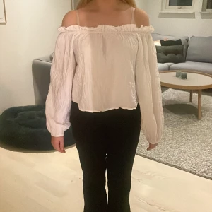  Vit offshoulder blus  - Säljer en superfin vit offshoulder blus med långa ärmar. Den har en krinklad textur och en söt volangdetalj vid halsen. Perfekt för både vardag och fest! Passar bra till jeans eller kjol.