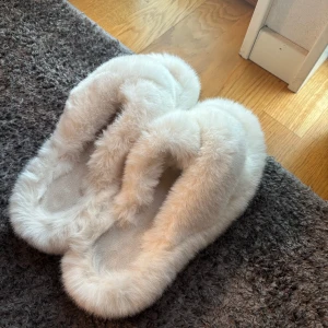 Vita fluffiga tofflor - Supermysiga vita tofflor i fluffigt material, perfekta för att hålla fötterna varma under kalla dagar. De har en hårdare sula och är i mycket bra skick (använda kanske en gång). Perfekta för hemmamys eller som en söt present!