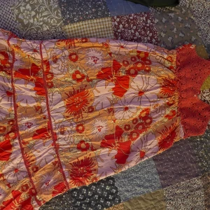 Färgglad blommig klänning - Säljer en superfin klänning med ett färgglatt blommigt mönster i rött, orange och vit. Den har en virkad topp med smala axelband och en luftig kjol. Perfekt för sommaren eller en dag på stranden. Klänningen är i bra skick!