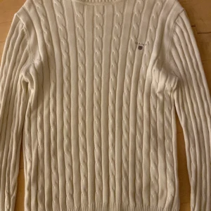 Vit stickad tröja från GANT - Säljer en stilren vit stickad tröja från GANT i storlek S. Tröjan har ett klassiskt kabelstickat mönster och långa ärmar, perfekt för kyliga dagar. Den är i mycket bra skick och passar både till vardags och lite finare tillfällen. Supermysig och tidlös design!