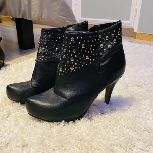 Svarta boots med nitar - Snygga svarta boots i skinn med klack och dragkedja på sidan. Stl 38!  De har coola nitar som ger en edgy look. Perfekta för höst och vinter, och funkar lika bra till fest som till vardags. Skorna har en spetsig tå och är i mycket bra skick.
