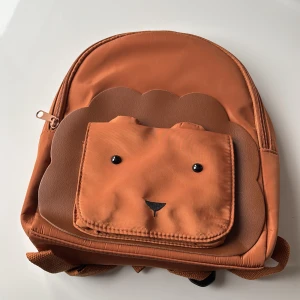 Brun ryggsäck med djurmotiv för barn. - Supergullig brun ryggsäck med ett sött djuransikte på framsidan. Perfekt för skolan eller utflykter! Den har justerbara axelremmar och en praktisk dragkedja. Tillverkad i slitstarkt syntetmaterial, vilket gör den både hållbar och lätt att rengöra. För barn.