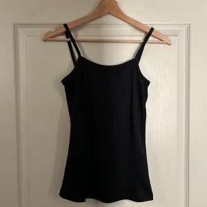 Svart linne - Säljer ett svart glansigt linne i mycket bra skick. Det är ärmlöst med smala axelband och har en tight passform. 